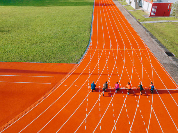 directamente por encima del punto de vista del dron, los atletas chinos asiáticos se alinean para prepararse para comenzar a correr en la pista y correr hacia la línea de meta por la mañana en el estadio de atletismo - pista de atletismo de tartán fotografías e imágenes de stock