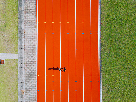 directly above drone point of view Asian chinese father son running at track and run towards finishing line in the morning at track and field stadium beside bleachers