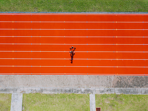 directly above drone point of view Asian chinese father son running at track and run towards finishing line in the morning at track and field stadium beside bleachers