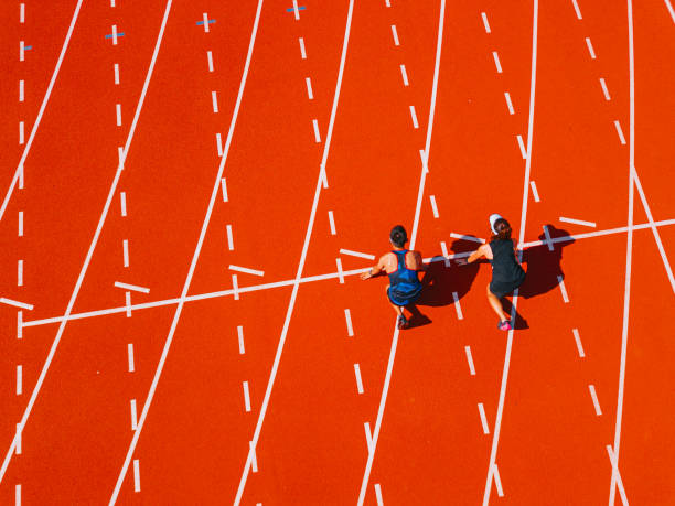 directamente por encima del punto de vista del dron, un par de atletas chinos asiáticos que se alinean para prepararse para comenzar a correr en la pista y correr hacia la línea de meta por la mañana en el estadio de atletismo - pista de atletismo de tartán fotografías e imágenes de stock