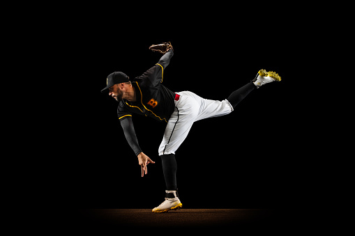 Preparing for double. Professional baseball player, pitcher in sports uniform and equipment practicing isolated on a black studio background. Competition, show and team sport concept. Copy space for ad.