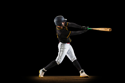 Professional baseball player, pitcher in sports uniform and equipment playing baseball isolated on black studio background in neon light. Competition, show and team sport concept. Copy space for ad.