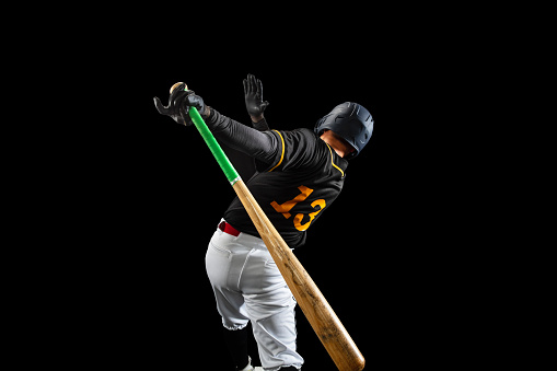 In action. Professional baseball player, pitcher in sports uniform and equipment playing baseball isolated on black studio background in neon light. Competition, show and team sport concept.
