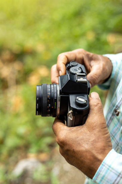 Close-up view from above in the hands of an elderly Thai man carefully holding an old film camera awaiting a photoshoot in a rural Thai area.