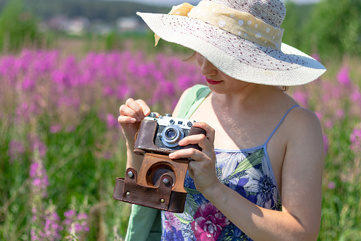 Portrait of a young woman with a camera in a hat in a field of red flowers on a hot summer day. Selective focus. Close-up