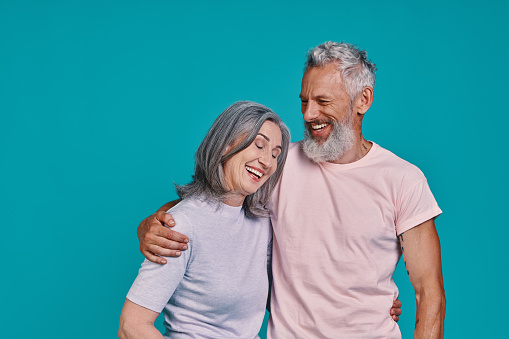 Happy senior couple smiling while standing together against blue background