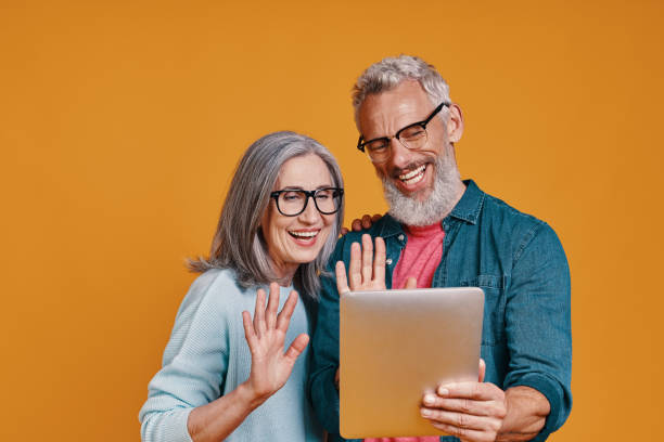 istock Happy senior couple smiling and using digital tablet and waving hands 1327098653