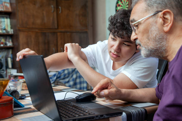 grandson is pointing to his grandfather at laptop monitor - senior adult technology child internet imagens e fotografias de stock