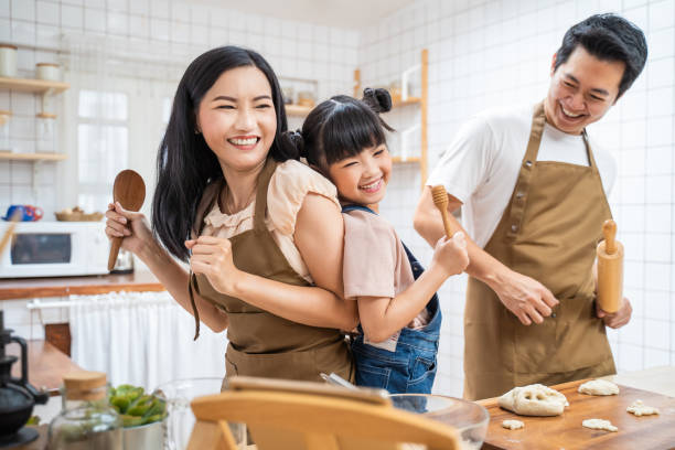 la famille asiatique heureuse reste à la maison dans la boulangerie cuisine et danse ensemble. pèreet mère passent du temps libre avec la petite fille fille faire de la nourriture, enfant profiter de la relation d’activité parentale à la maison. - mother cooking daughter child photos et images de collection