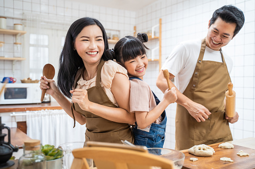 Asian happy family stay home in kitchen bake bakery and dance together. Fatherand mother spend free time with young little girl daughter make food, Kid enjoy parenting activity relationship in house.