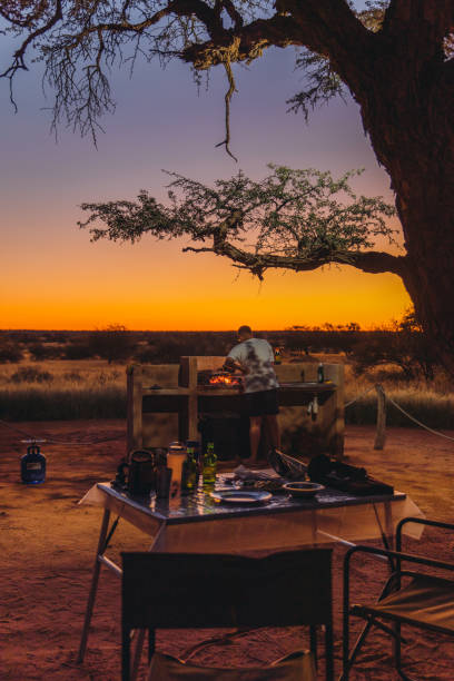 istock Young man traveler having bbq dinner outdoors at the campsite during bright sunset in Kalahari desert, Namibia 1327104087