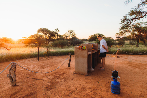 Man tourist preparing food on the campfire camping in the wild desert during sunny summer sunrise in Namibia, Southern Africa