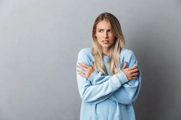 Portrait of an annoyed young blonde girl shaking from cold isolated over gray background