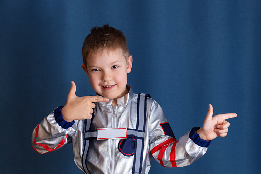 Astronaut concept. Portrait of cute little boy in space suit pointing to the side. Isolated background with copy space.