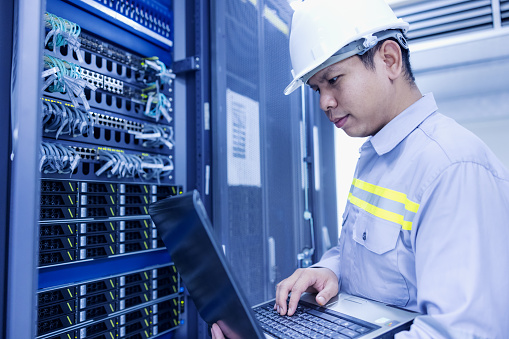 Network administrator holding laptop in hand working Configuration with core switch on rack cabinet in data center