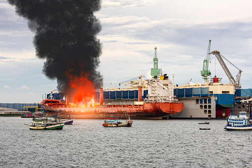 Large general cargo ship for logistic import export goods and other the explosion and had a lot of fire and smoke while moored at harbor in afternoon