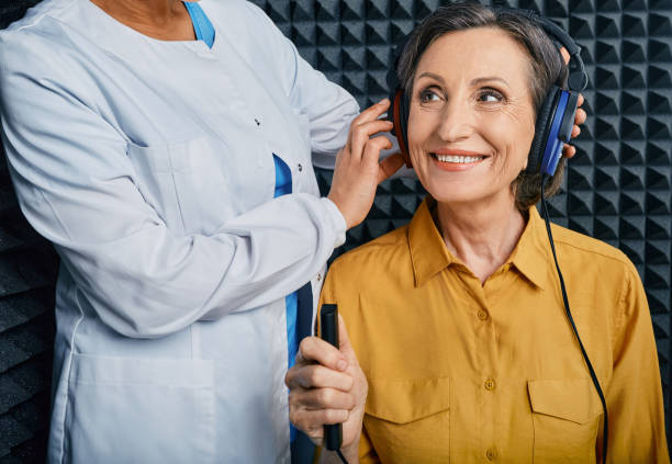 ritratto donna anziana con sorriso dento bianco durante il check-up dell'udito con ent-doctor presso la cabina audiometrica insonorizzata utilizzando cuffie audiometriche e audiometro - esame otorino foto e immagini stock