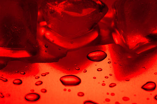 Red ice cubes on a reflecting table with drops of water close-up