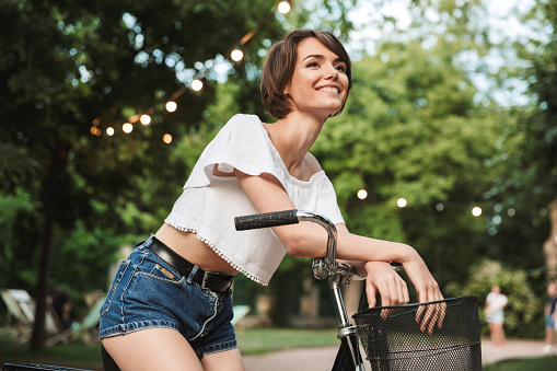 Pretty young girl in summer clothes sitting on a bicycle at the park