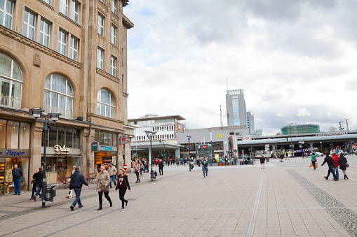 View from city street Kettwiger Strasse over square Willy-Brandt-Platz to main station Essen in autumn season. Many people are walking around in any direction and also in front of station. Behind station is Evonik building