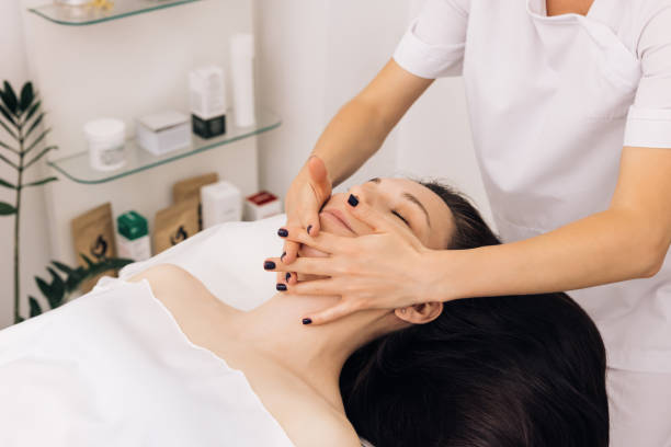 massage visage dans un salon de spa de beauté. femme caucasienne recevant un massage facial dans un salon esthétique. spa massage facial. soins du corps, soins de la peau, bien-être, bien-être, concept de traitement de beauté - esthéticienne photos et images de collection