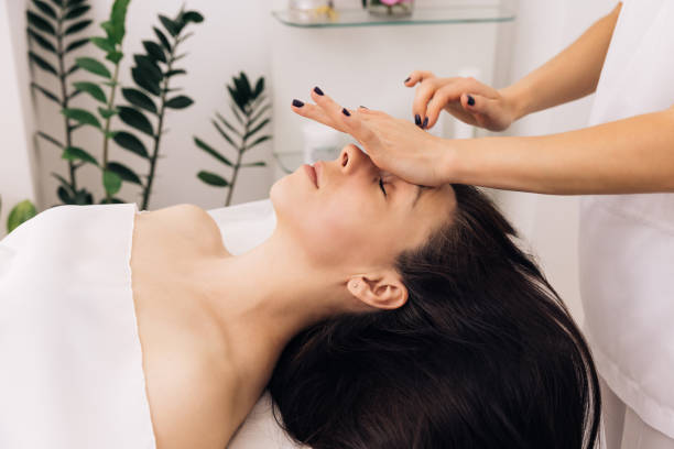 close up of young girl receiving a facial massage and spa treatment for perfect skin in a luxury wellness center. caucasian woman lying on spa bed get facial massage from massage therapist at clinic - massage therapist massaging sport beautician imagens e fotografias de stock