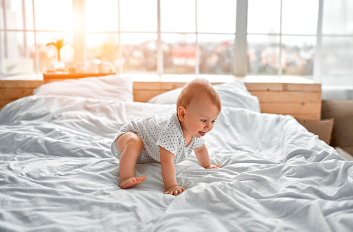 Adorable baby boy in white sunny bedroom. Newborn child relaxing in bed. Nursery for young children. Textile and bedding for kids. Family morning at home. New born kid during tummy time.
