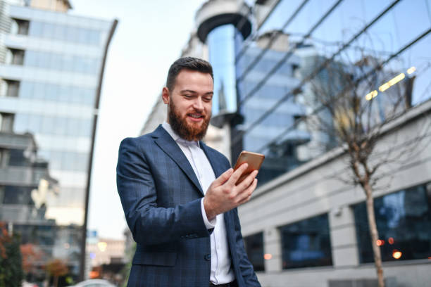 istock Bearded Elegant Male Smiling While Looking Up Location On Dating App 1327128826