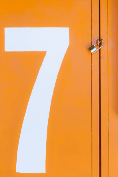 istock Orange closed metal gate with padlock with a white number 7 1327130756
