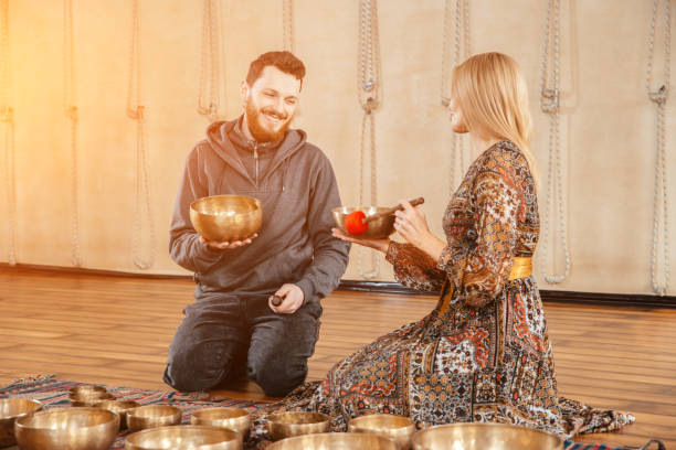 frau und mann spielen auf einer tibetischen klangschale für klangtherapie sitzen dim im yoga-studio. sonnenlichteffekt - third place audio stock-fotos und bilder