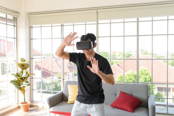 istock Young Asian man getting experience with VR virtual reality headset or 3D glasses in living room at home. technology, gaming, entertainment concept 1327132537