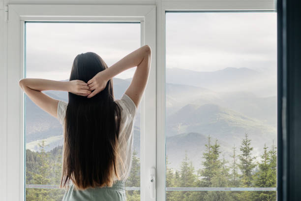 istock Young woman standing near window, hands above head 1327134781