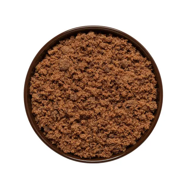 Photo of Cane brown muscovado sugar in a bowl isolated on white background. Top view. Indian sugar.