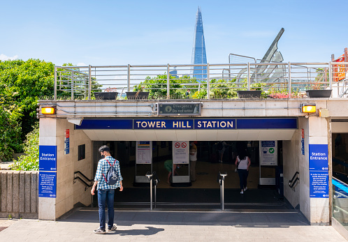 Passengers entering Tower Hill underground station in central London on a sunny spring day. Some wear face coverings as protection during the COVID-19 pandemic, and everywhere is very quiet.