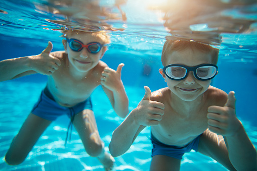 Little boys aged 6 swimming underwater. The boys are smiling at the camera showing thumbs up.
Nikon D800