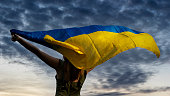Woman holding ukrainian flag on dark cloudy sky background.