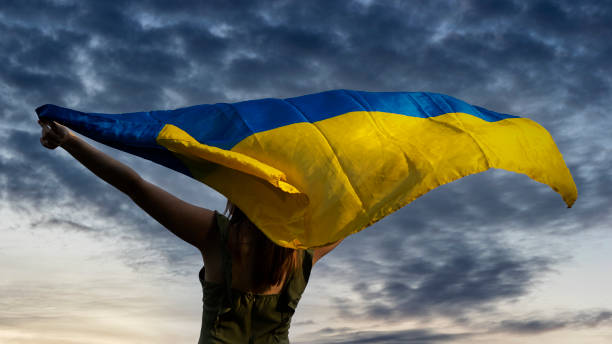 Woman holding ukrainian flag on dark cloudy sky background. stock photo