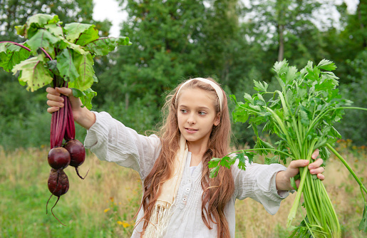 girl with fresh beets and celery in her hands on a background of greenery, outdoors