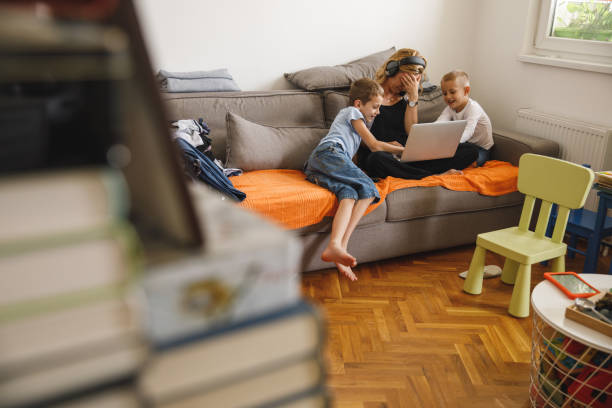 istock Woman holding head in hands while her sons are interrupting her work 1327147868