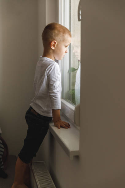 istock Distraught little boy looking through the window 1327147924