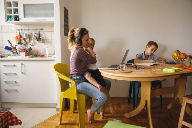 Woman getting annoyed by her son who is interrupting her work video conference Wide shot of mid adult woman getting annoyed by her little son, sitting on her lap, who is interrupting her work video conference while her older son is writing his homework. lifehack stock pictures, royalty-free photos & images
