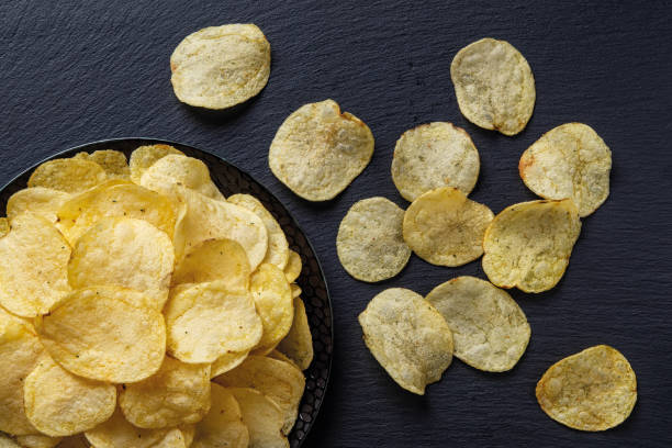 istock Top view on a crunchy potato chips on a black ceramic plate over black slate surface. Tasty snack of deep-fried thin potato slices. Ready to eat fastfood, unhealthy eating and junk food. 1327156697