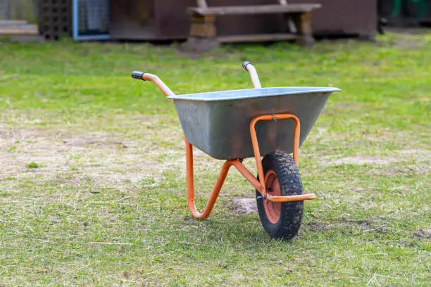 Photo of wheelbarrow closeup on a lawn in garden, garden maintenance, work in garden