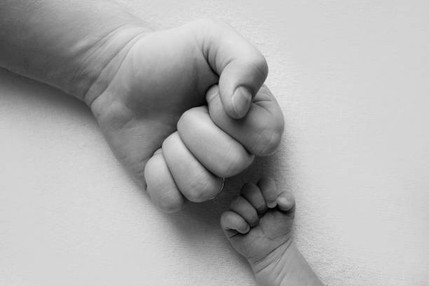tata i nowo narodzony syn chłopiec trzymają ręce w pięści, małych i dużych pięściach. ojciec i syn, pierwszy bokserski cios. czarno-białe zdjęcie. - newborn human hand baby father zdjęcia i obrazy z banku zdjęć