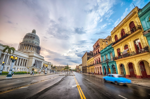 blue classic car riding against historic buildings and Capitolio government in the colorful streets of la Havana at sunset, Cuba