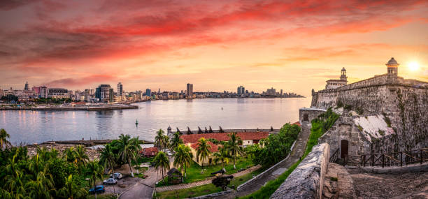 Havana city by sea against sky during sunset. Cuba Havana, Cuba skyline at sunset seen from El Morro Fortress. The Malecon seafront promenade and Havana Vieja illuminated at dusk, El Morro Lighthouse is visible in the foreground, old havana stock pictures, royalty-free photos & images