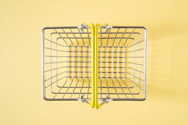 Empty shopping basket with yellow handle on beige background. Top view.