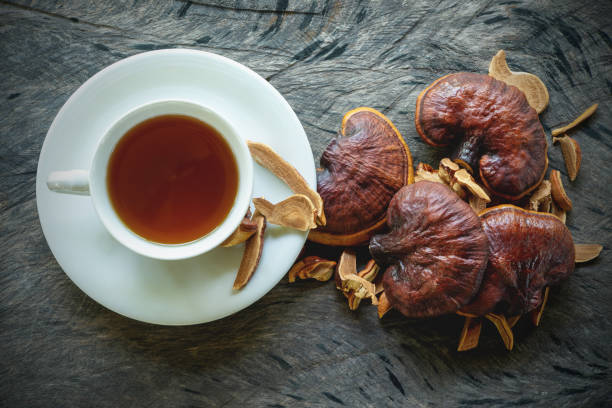 Cup of reishi tea and fresh Lingzhi mushroom. Cup of reishi tea and fresh Lingzhi mushroom with slice on dark wooden floor. (Ganoderma Lucidum). Chinese traditional medicine and nutritive value. ganoderma lucidum stock pictures, royalty-free photos & images