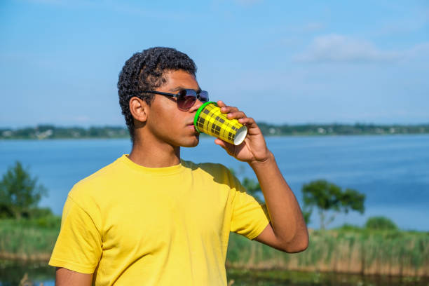 African American man in sunglasses enjoying the taste of coffee outdoor in summer near river.