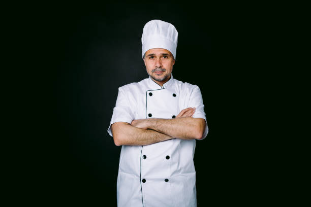 istock Chef cook wearing cooking jacket and hat, arms crossed, on black background 1327176882